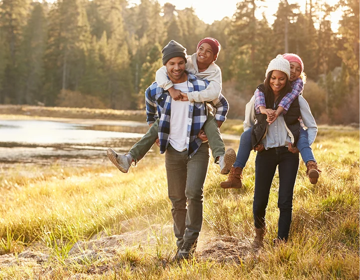 Parents give their kids piggy back rides in the autumn time near a mountain lake